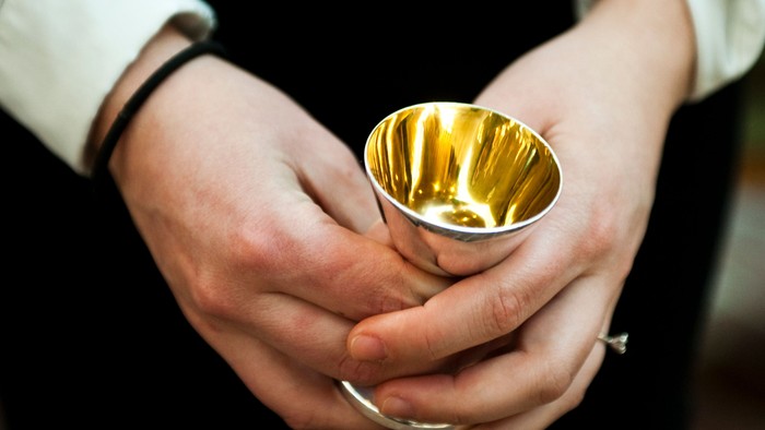 Hænder, der holder en gylden kalk eller bæger, sandsynligvis brugt i en religiøs eller ceremoniel sammenhæng.