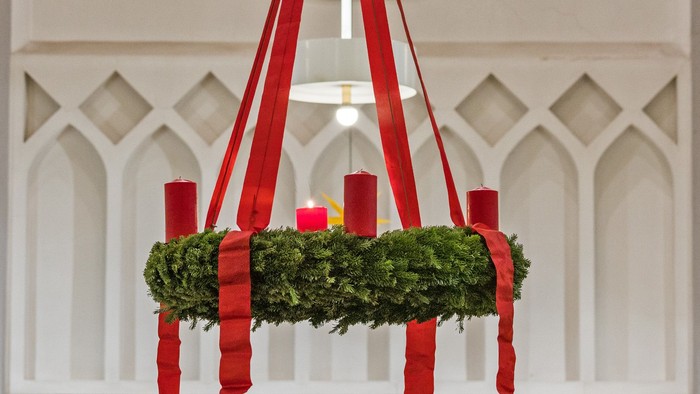 Ein Kranz mit Kerzen, die an roten Bändern hängen.