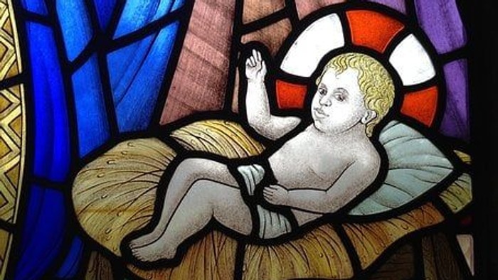 Das Bild zeigt ein buntes Kirchenfenster mit einem darstellten Baby.