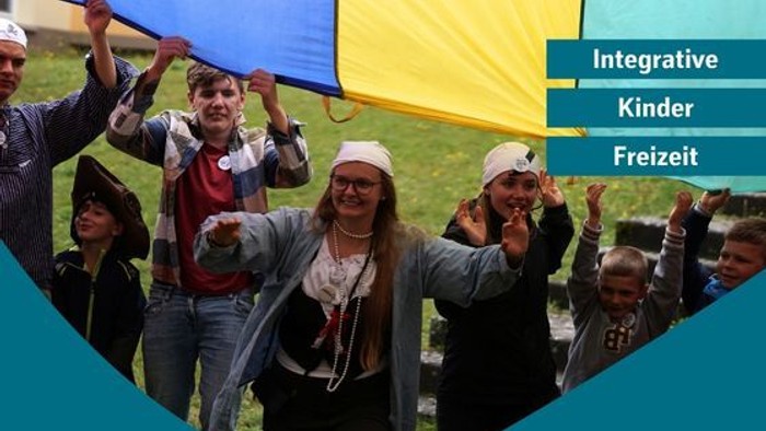 Eine fröhliche Gruppe von Menschen hält ein großes gelbes Banner und feiert integrative Freizeitaktivitäten für Kinder während einer Veranstaltung.