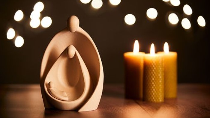 Eine Kerze und eine Figur auf einem Holztisch vor buntem Hintergrund