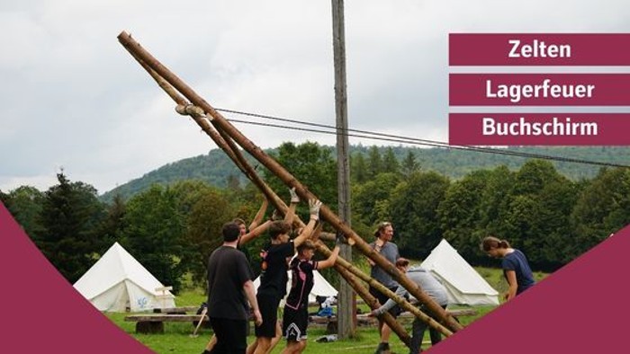 Gruppe baut eine große Holzrahmenkonstruktion für Campingaktivitäten mit Zelten und Details für Outdoor-Veranstaltungen.