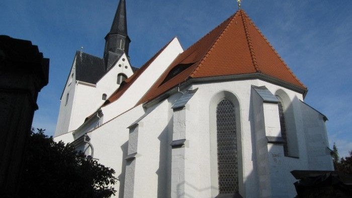 Weiße Kirche mit rotem Dach und hohem Turm vor blauem Himmel