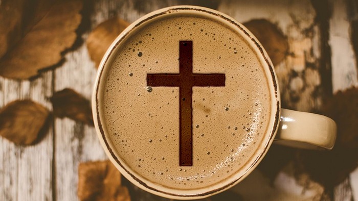 Eine Tasse Kaffee mit einem kreuzförmigen Muster im Schaum, platziert auf einer Holzfläche mit Blättern.