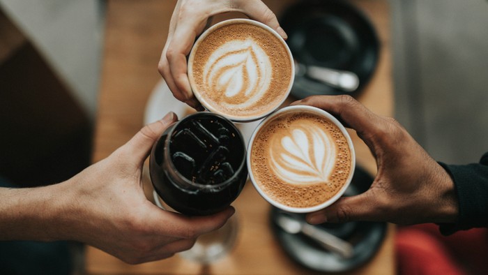 Vier Hände halten Kaffeetassen und Tumbler zum Anstoßen