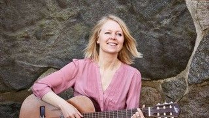 En kvinde med blond hår spiller guitar i naturen.