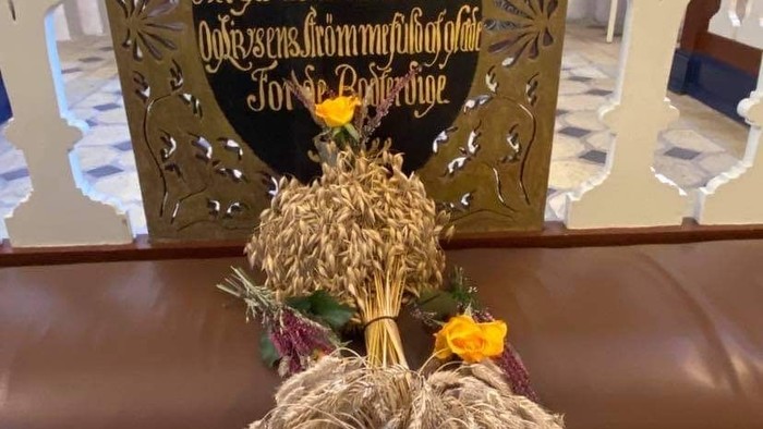 En blomsterarrangement foran et præsteembed med indskrift på latin