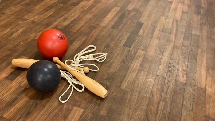 Bunte Gymnastikbälle und Holzstäbe mit befestigten Springseilen auf einem Holzboden.