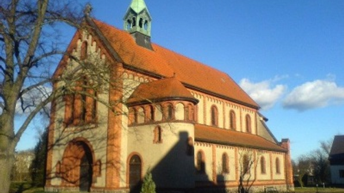 Kirchengebäude mit rotem Dach und grünem Turm im Sonnenlicht