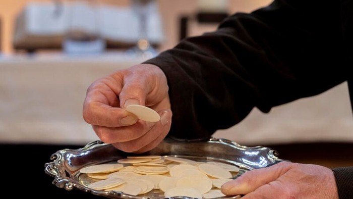 Hände, die Brotscheiben auf ein gemeinschaftliches Silbertablett während eines Rituals oder einer gemeinsamen Veranstaltung legen.