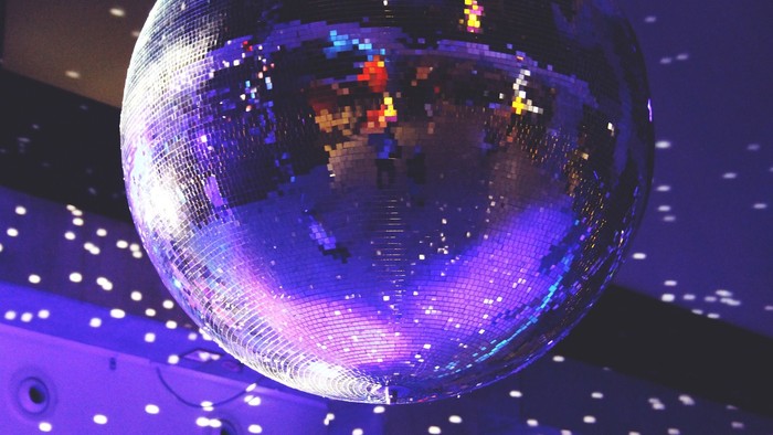Ein großer Diskokugel an der Decke unter bunten Lichtern.