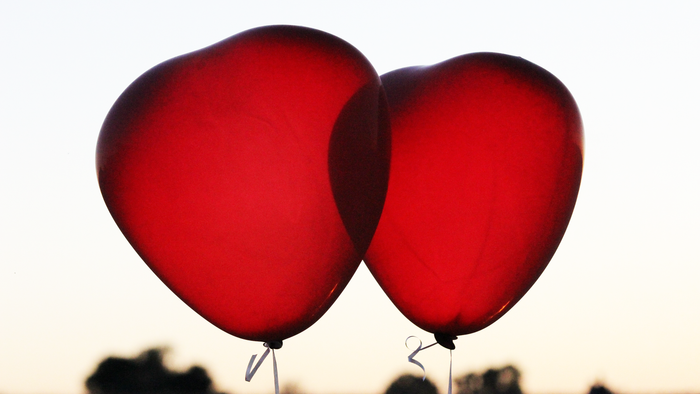 Zwei herzförmige Luftballons vor Abendhimmel mit Stadtsilhouette