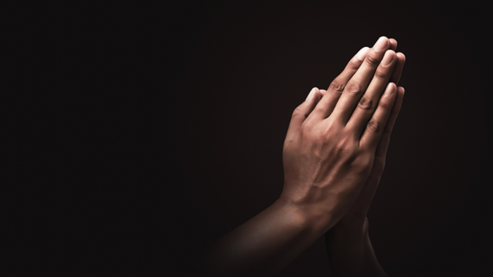 Hands clasped together in prayer against dark background.