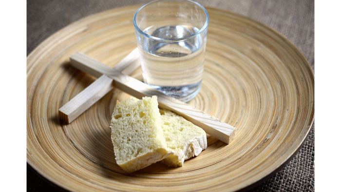 Einfaches Essen aus Brot, Käse, Crackern und einem Glas Wasser auf einem Holztablett.
