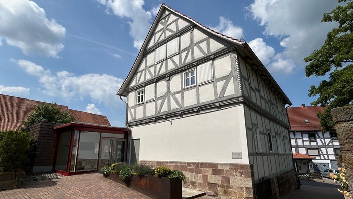 Traditionelles Fachwerkhaus mit modernem Glasanbau, umgeben von einem Ziegelhof und Grünflächen.