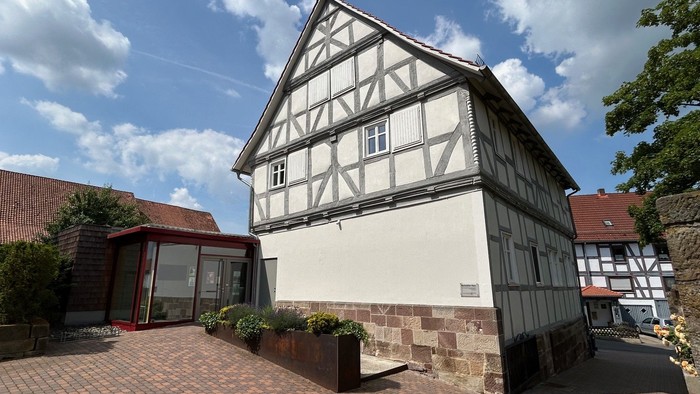 Traditionelles Fachwerkhaus mit modernem Glasanbau, umgeben von einem Ziegelhof und Grünflächen.