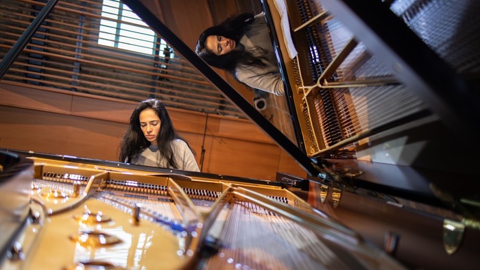 Zwei Personen, die ein großes, komplexes mechanisches Instrument beobachten und spielen, das einem Klavier ähnelt.