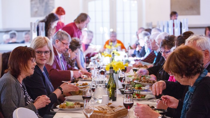 En gruppe mennesker sidder sammen og spiser på et langbord med mad og drikkevarer