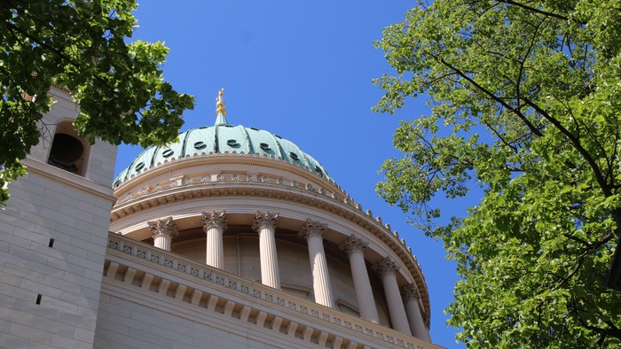 Das Bild zeigt eine Kuppel eines Gebäudes mit Säulen und grünen Bäumen im Vordergrund