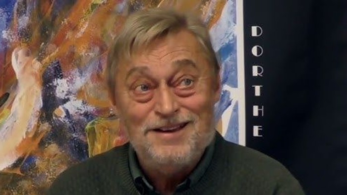 En mand står ved siden af et abstrakt, farverigt maleri med navnet 