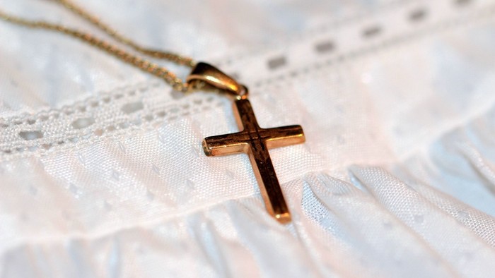 En guldkæde med et small cross hænger på et hvidt spandextrøje.