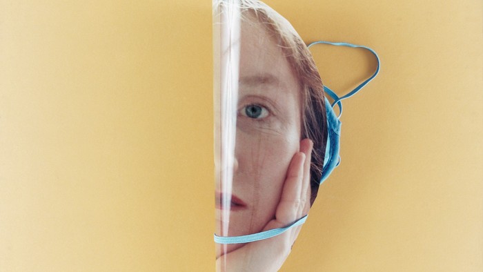 Eine Nahaufnahme einer Person, die ein durchsichtiges Gesichtsschild mit einem blauen Gummiband über einer Maske trägt.