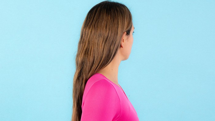 Eine Person mit langen glatten Haaren in einem knallrosa Oberteil vor einem einfarbig blauen Hintergrund.