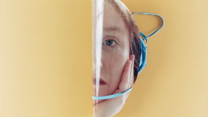 Eine Nahaufnahme einer Person, die ein durchsichtiges Gesichtsschild mit einem blauen Gummiband über einer Maske trägt.