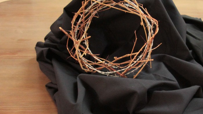 Ein geflochtener Kranz liegt auf schwarzem Stoff auf einem Holztisch.