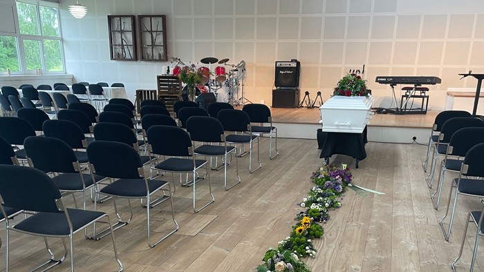 Elegant begravelseslokale med gang prydet af farverige blomsterdekorationer og pænt opstillede stole.