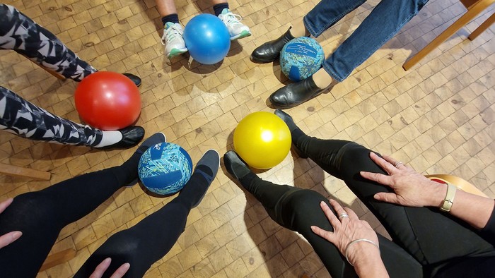 Eine Gruppe von Menschen sitzt im Kreis und hält bunte Bälle.