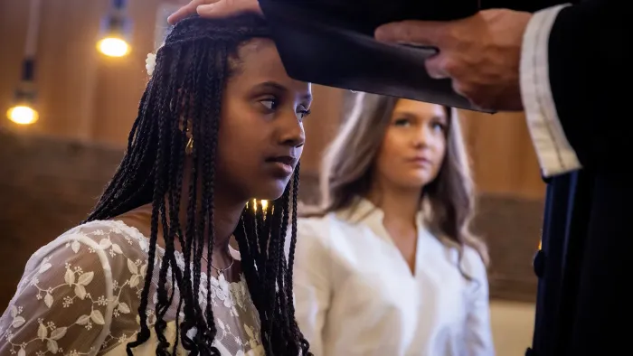 En kvinde med fletninger modtager en velsignelse eller hårjustering under en ceremoni, mens andre iagttager.