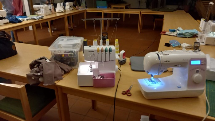 Ein Nähkursraum mit mehreren Tischen, Nähmaschinen und Zubehör.
