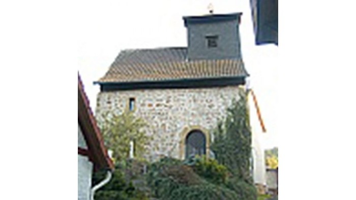 Kleine Steinkirche mit bogigem Eingang, umgeben von Grünflächen.