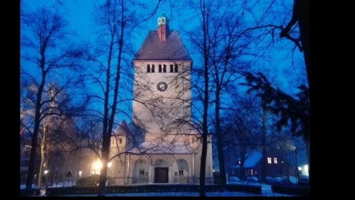 Ein beleuchtetes Kirchengebäude bei Nacht mit Uhrenturm und kahlen Bäumen