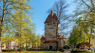 Ein alter Turm steht in einem Park mit Bäumen und Häusern.