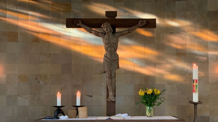 Das Bild zeigt eine Kreuzigungsstatue in einer Kirche mit Kerzen und Blumen.