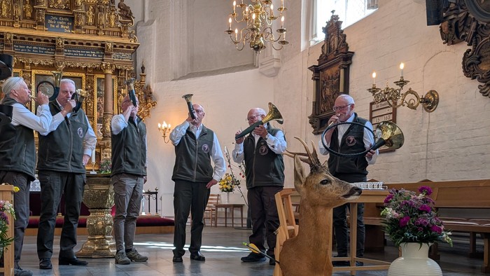 En gruppe mænd i en kirke løfter hænderne, mens en hjortestatue vises under en ceremoni.