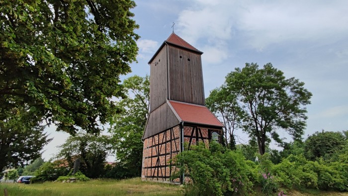 Ein hölzernes Gebäude mit einem hohen Turm, umgeben von Bäumen und Gras.
