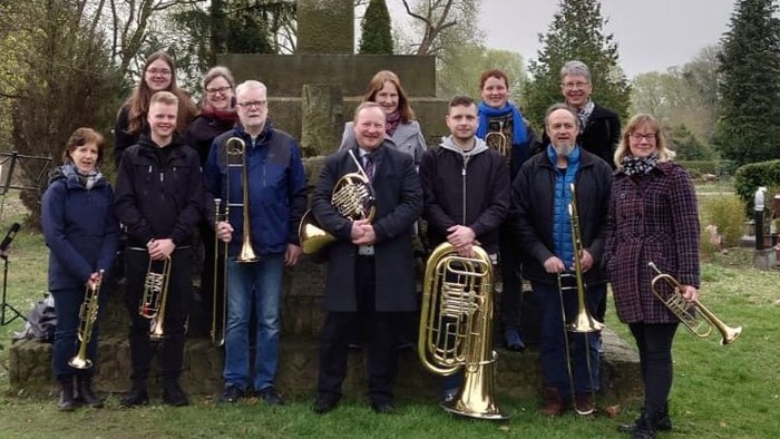 Ein Musikensemble posiert vor einem großen Kreuz in einem Park