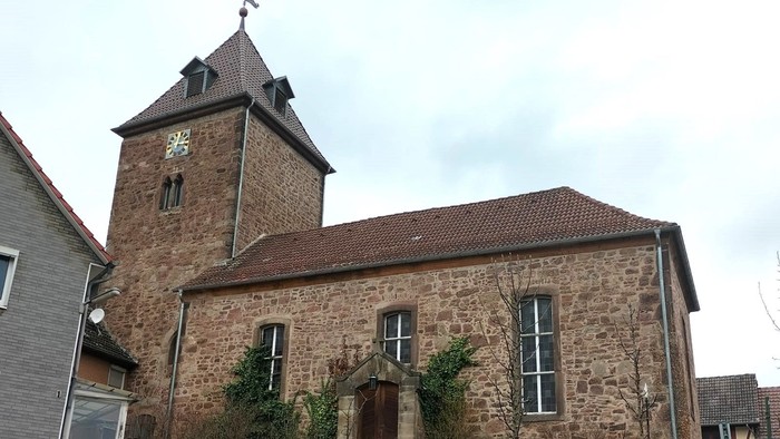 Steinkirche mit hohem Uhrturm und Holzzaun.
