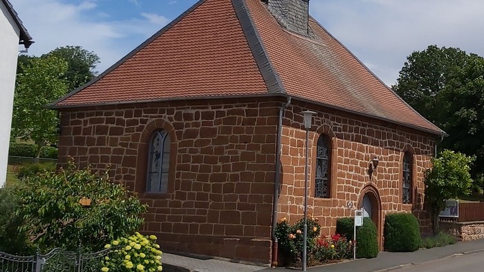Kleine Backsteinkirche mit rotem Dach und Glockenturm.