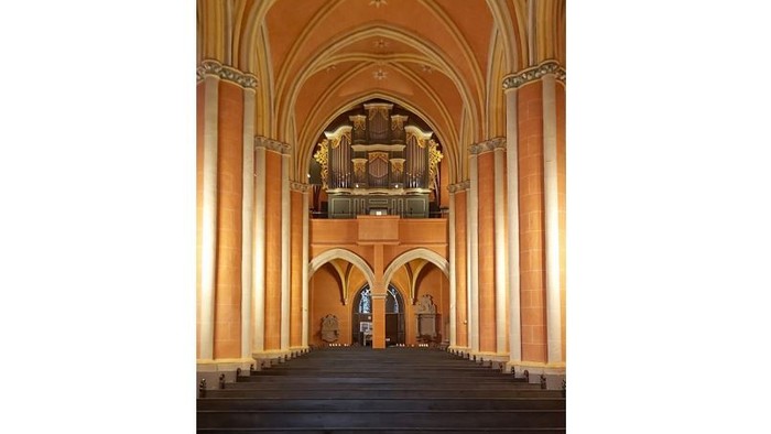 Kircheninneres mit hohen Bögen, Säulen und einer Orgel.