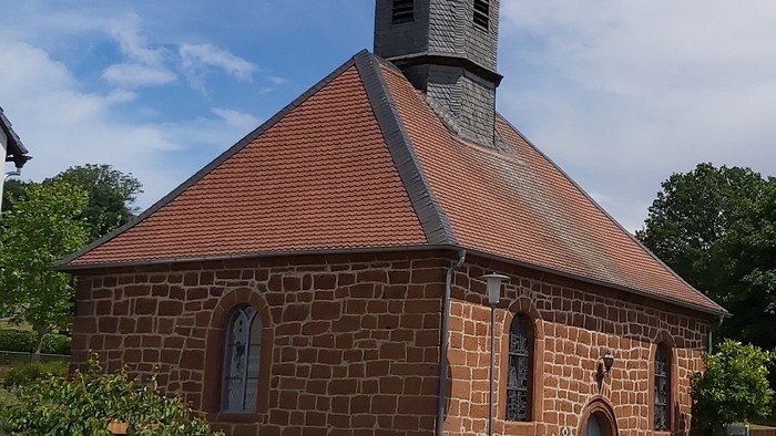 Kleine Backsteinkirche mit rotem Dach und Glockenturm.