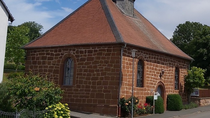 Kleine Backsteinkirche mit rotem Dach und Glockenturm.