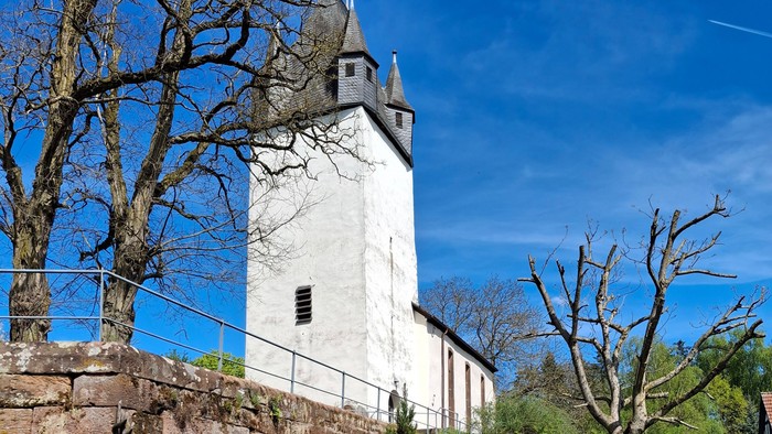Historischer Steinturm mit Treppe, umgeben von Grünflächen und Bäumen.