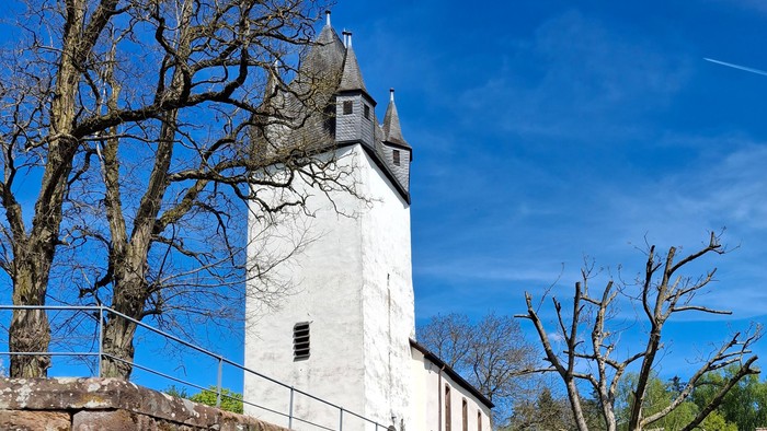 Historischer Steinturm mit Treppe, umgeben von Grünflächen und Bäumen.
