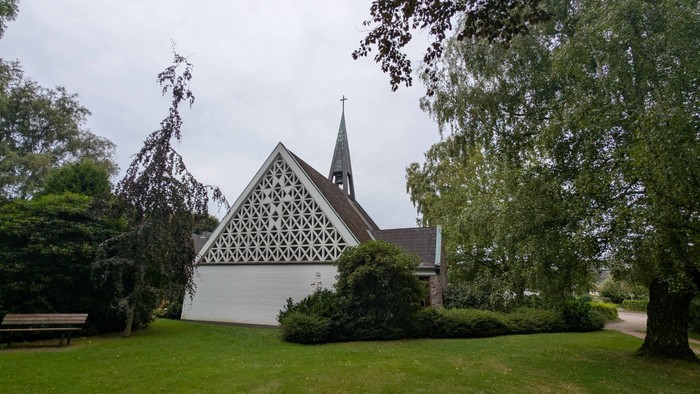 Kleine Kirche mit spitzem Turm und weißem Zaun in grünem Garten
