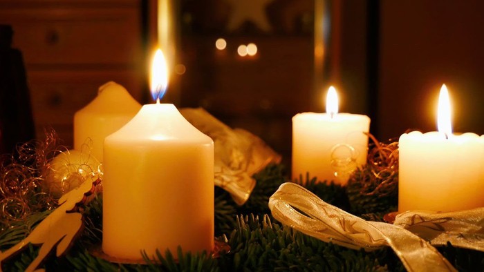 Drei brennende Kerzen auf grünem Kranz mit Weihnachtsdekoration