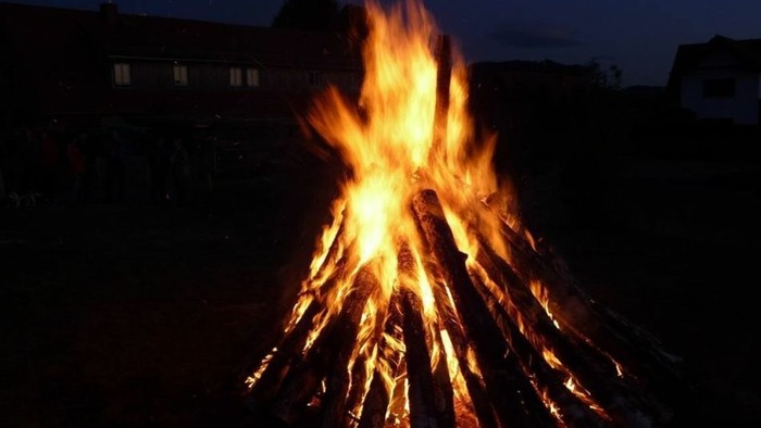 Ein großes Lagerfeuer brennt in der Dunkelheit vor Häusern.